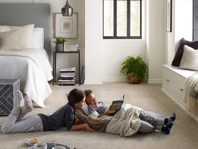 two kids laying in bedroom reading a book