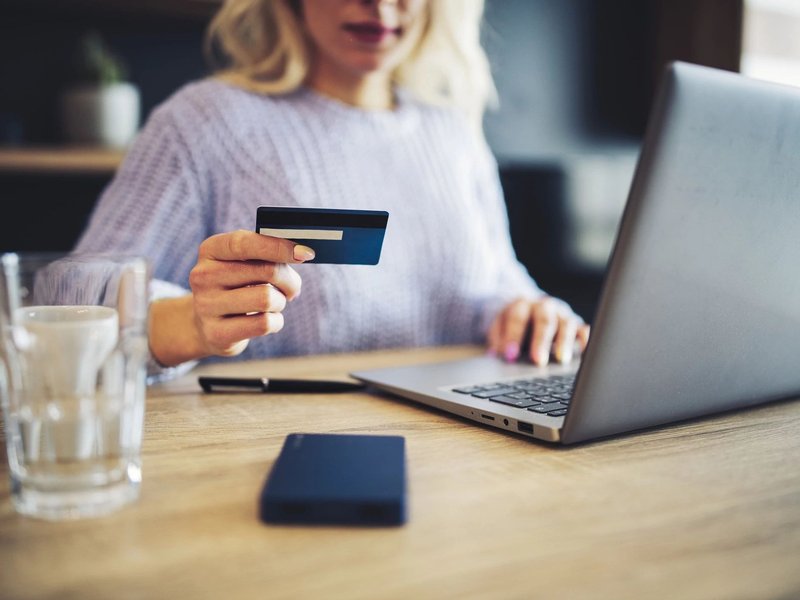 woman holding credit card while using laptop